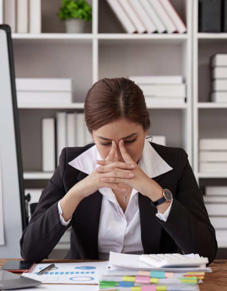 Illustration of an overwhelmed employee at a desk, showing signs of burnout and stress with paperwork, fatigue, and anxious expression.